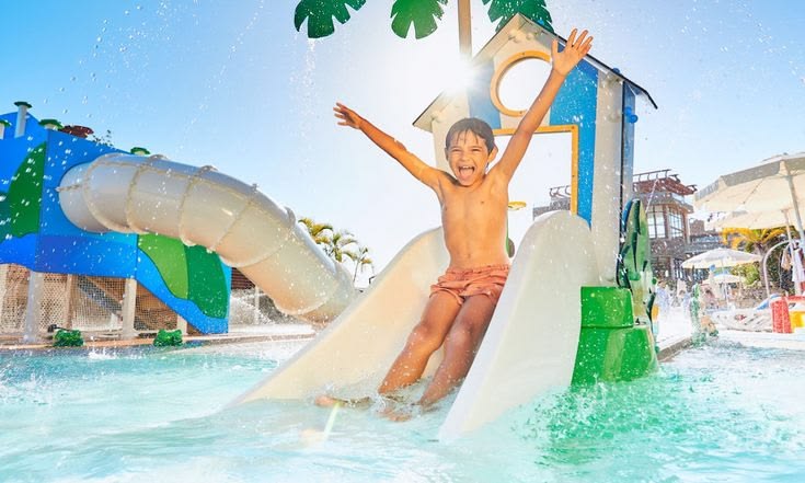 Happy boy in sunglasses riding a yellow tube in a splash of water